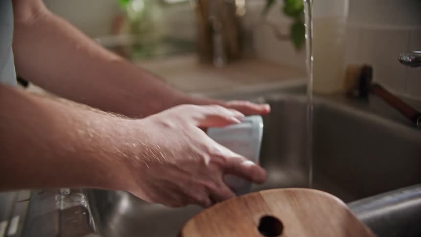 A man washes a glass bowl in the kitchen sink and places it on the counter to dry