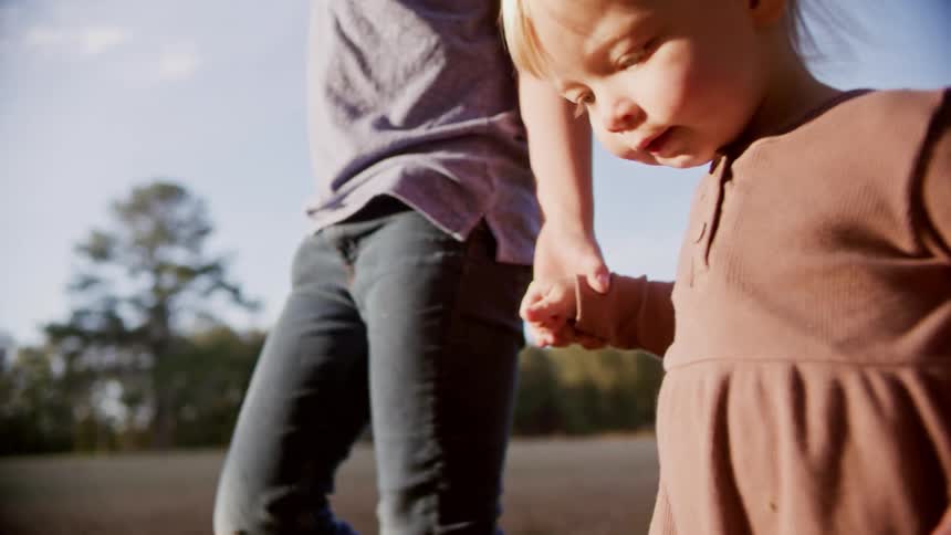 A person holding a little girls hand and walking with trees the sky and clouds in the background