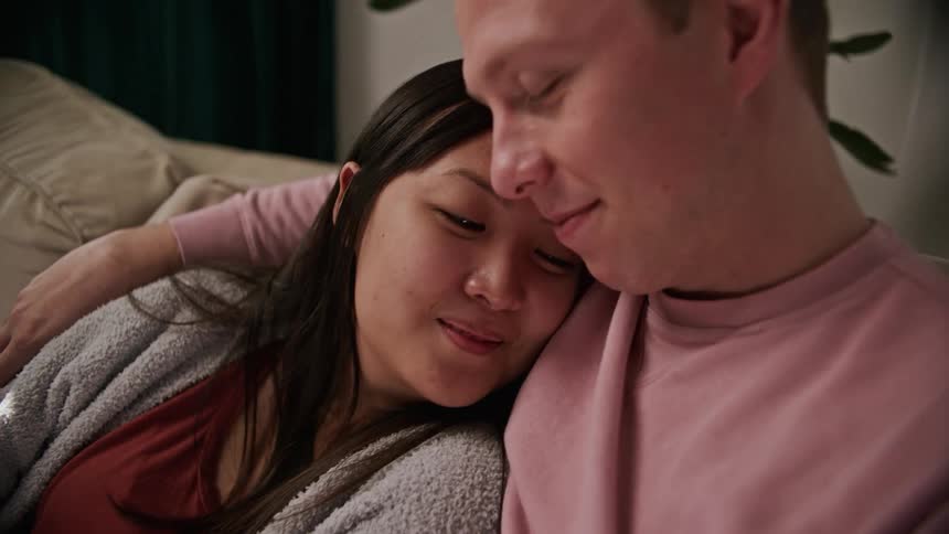 A woman rests her head on her boyfriends chest as they cuddle on a couch