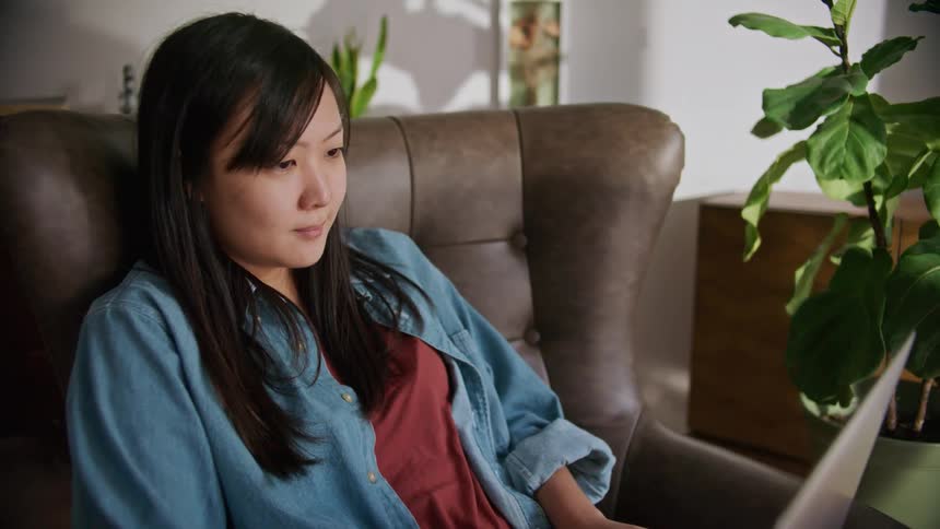 A woman sits in a leather chair while looking at the screen of her laptop computer
