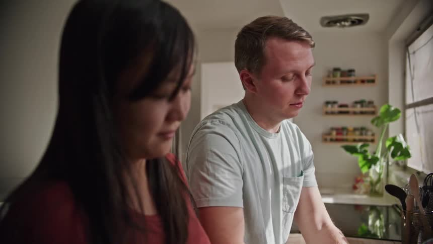 A man and woman stand at the kitchen sink as he washes dishes and she dries them