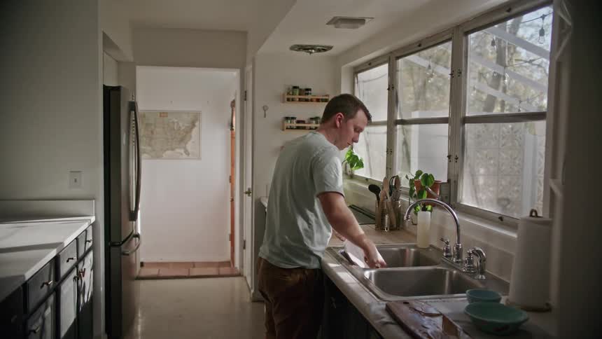 A man does dishes at his kitchen sink at home