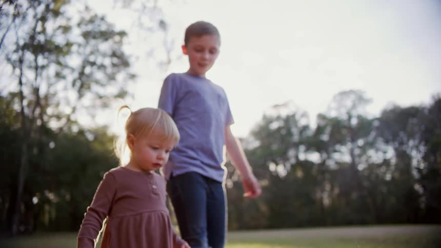 Brother and sister walking on the green grass in the backyard at sunset