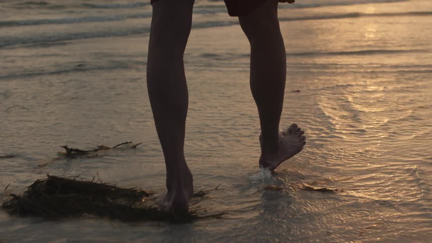 A man wades in the ocean at sunset