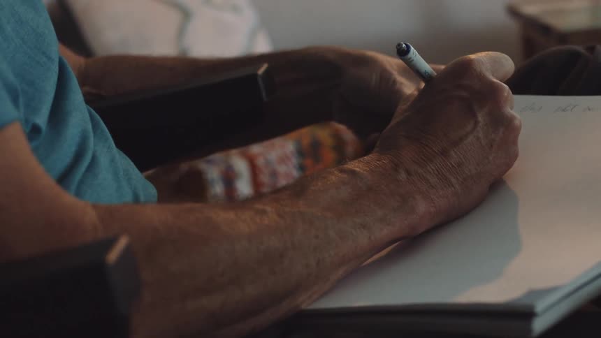 A man sits and writes in a notebook at home