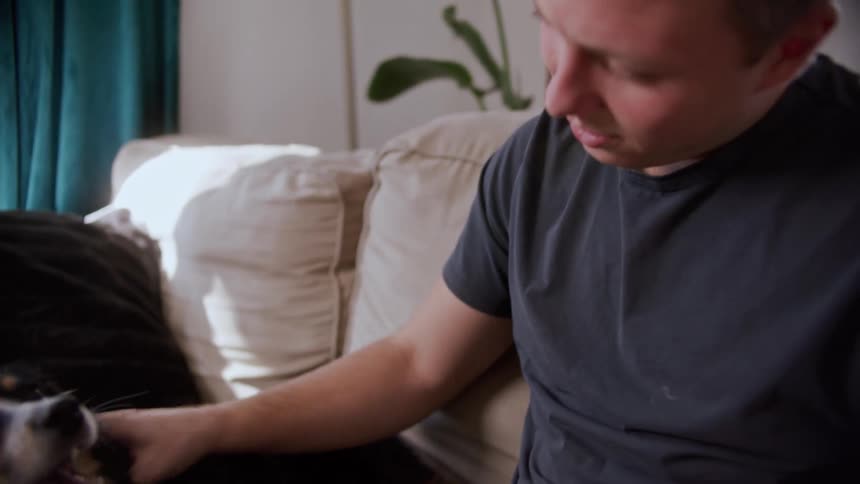 A man sitting on a couch petting his dog