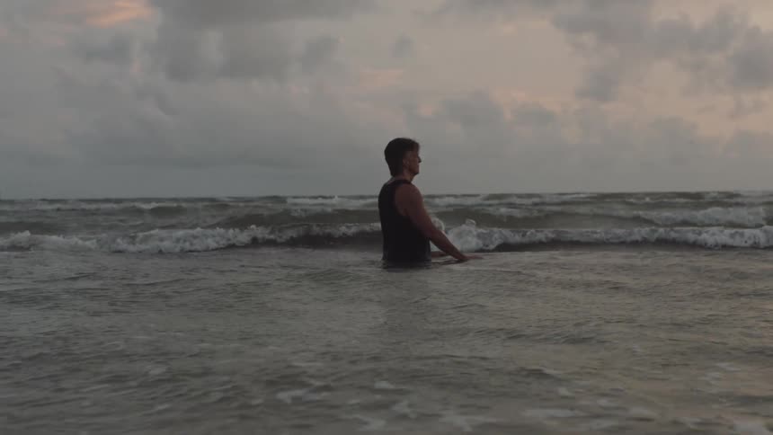 A man standing in the ocean at dusk