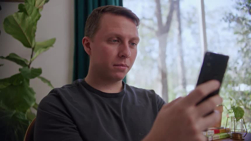 A man in a room sitting on a chair looking at a smart phone