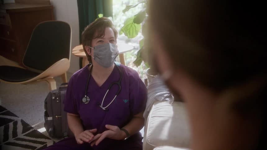 A nurse wearing a face mask talking to a patient during a home visit