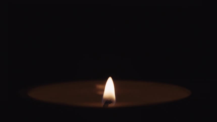 A small flame atop a candle begins to burn and illuminate the darkness