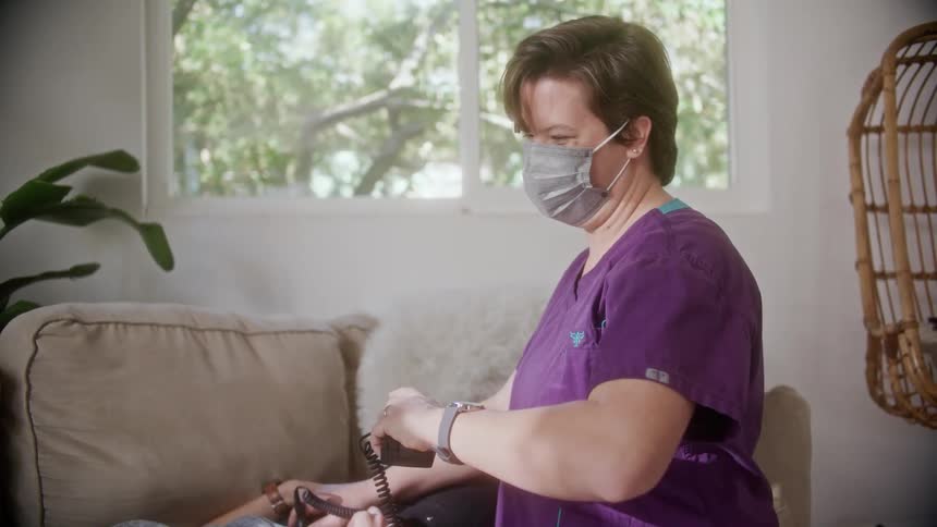 A nurse talks with a patient a she examines her in her home