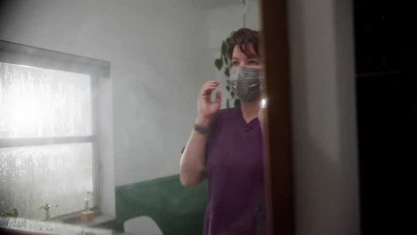 A nurse putting on a mask in front of a mirror