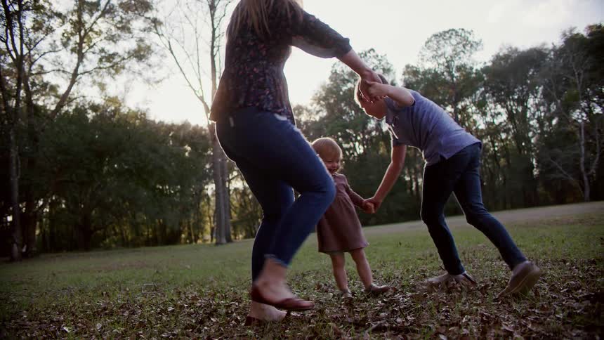 A mother holds hands with her son and daughter and they spin in a circle outside