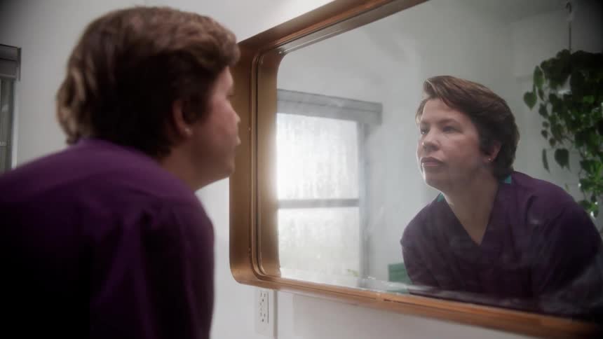 A woman looks at her reflection in a large mirror while washing her hands