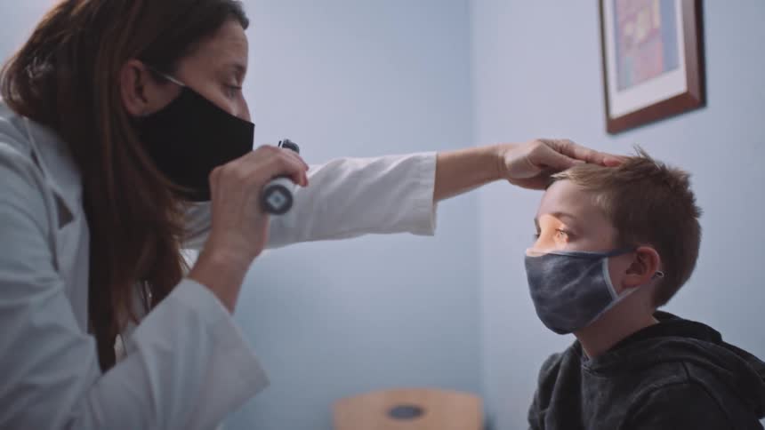 A doctor has a young boy follow the light as she examines his eyes during a checkup