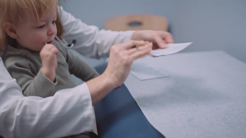 Doctor wearing face mask holds toddler as she writes