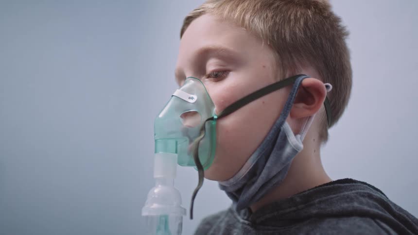 A boy with a respirator with smoke sitting in a room with a wall in the background