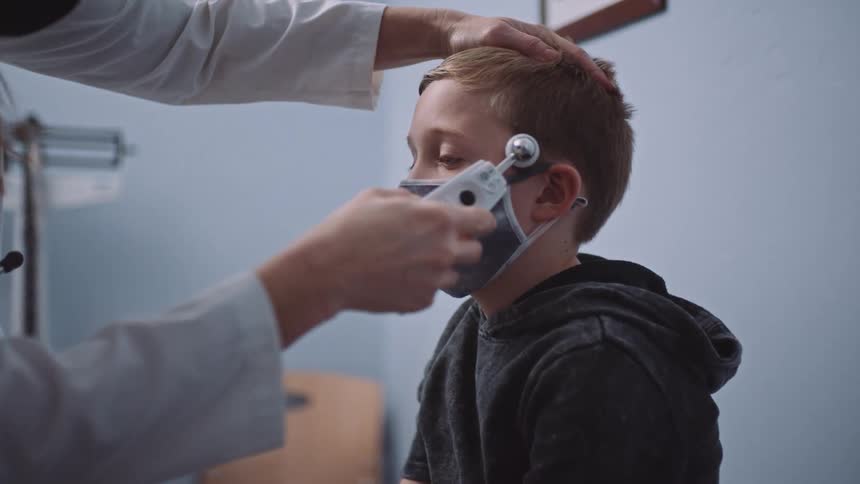 A doctor swipes a thermometer across a boys forehead as he sits on the exam table