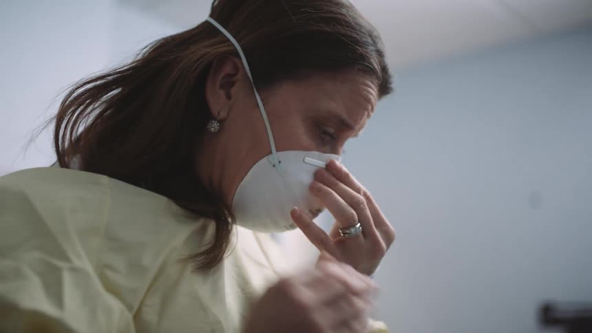 A woman puts on a medical face mask and glasses in a medical office environment