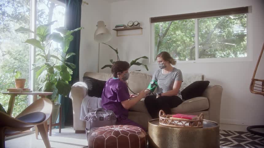 A nurse taking the blood pressure of another woman on the couch