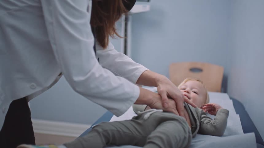 A female doctor palpates the belly of a smiling child and pauses to touch the childs head