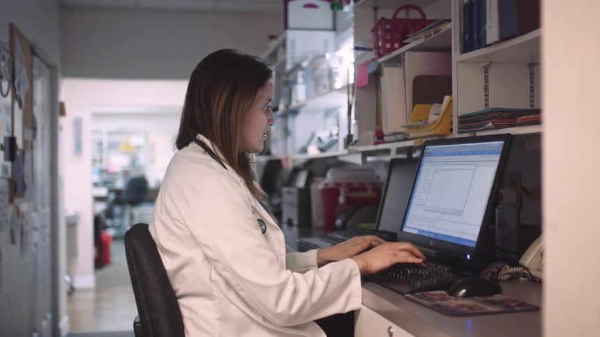 A doctor typing at a computer while wearing a lab coat