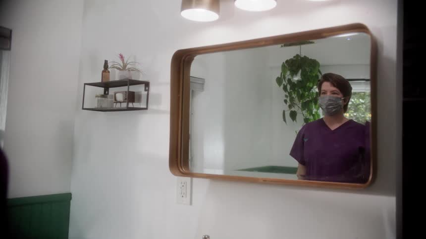 A woman adjusts her mask in the mirror