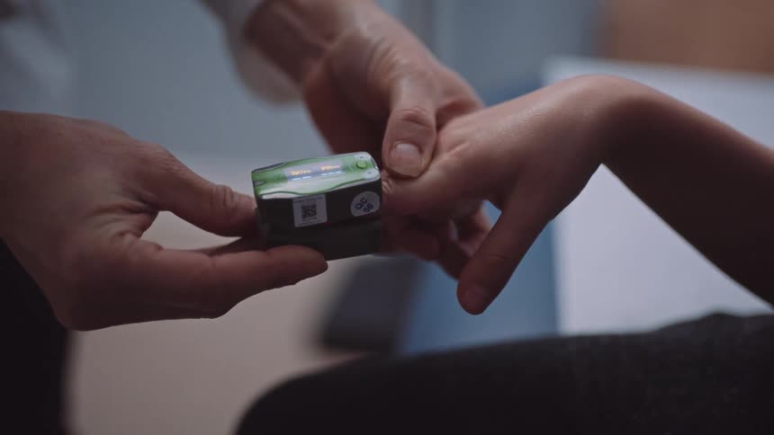 A doctor uses a finger clip device to measure a boys pulse and oxygen level in an exam room