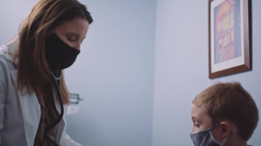 A female physician places a blood pressure cuff on the arm of a boy in an exam room