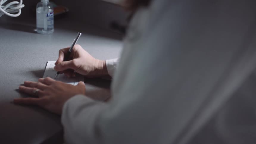 A physician hand writes with a pen on her prescription pad