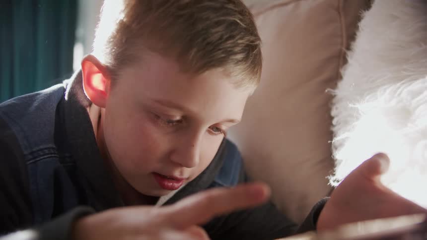 A child laying on a bed playing with a tablet