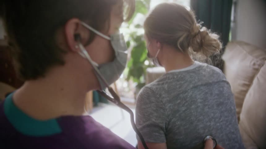 A nurse at a patients home uses a stethoscope to listen to the patients back