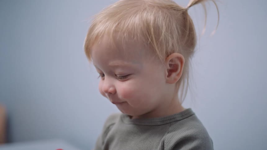 A little girl sitting in a clinic eating a lollipop with a chair in the background