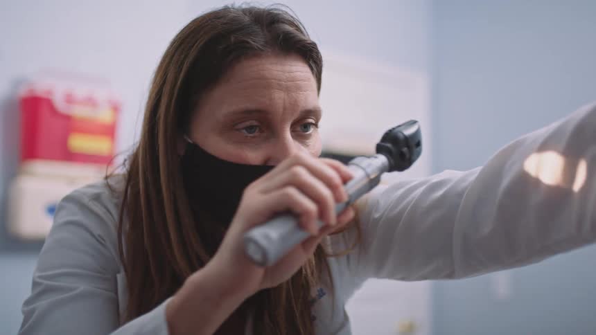 A doctor uses a lighted tool to check the eyes of a young patient