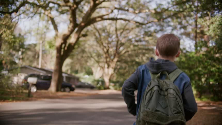 Young boy carrying a backpack walking on the streets of the neighborhood at daytime