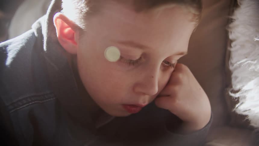 A young boy lies on a couch and plays on a tablet