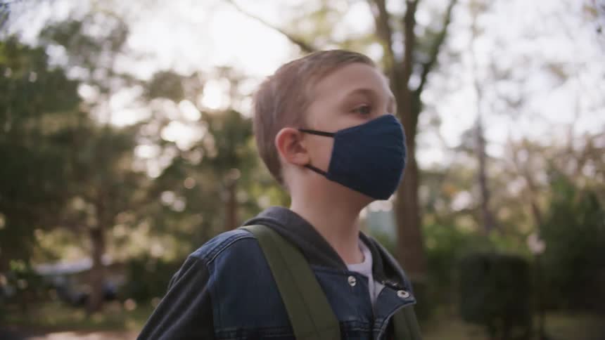 A young boy wearing a face mask walks along a street in a residential neighborhood