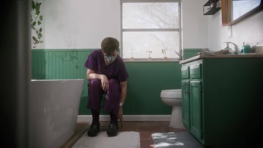 A woman sits in a chair in her bathroom and puts on black clogs