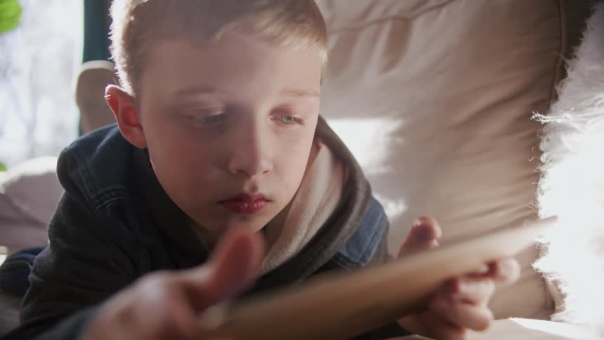 A child reading on a tablet while laying on a bed