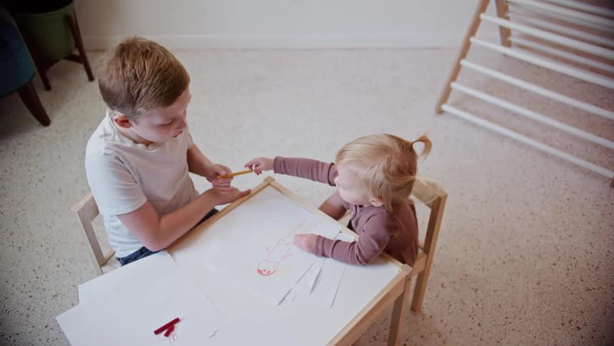 A little girl hands a crayon to her brother so he will help her draw