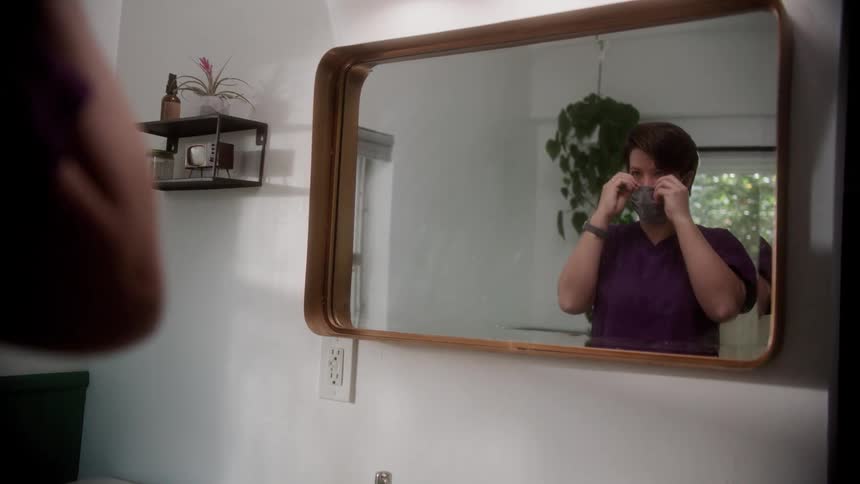 A nurse putting on a mask in front of a mirror