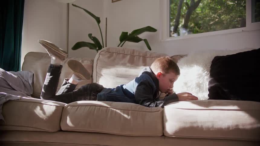 A boy is laying on the couch reading something