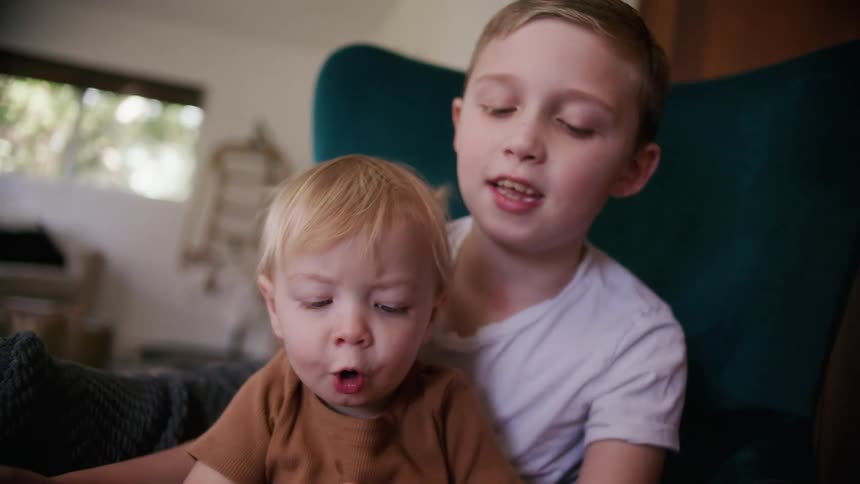 Brother and sister reading a book sitting in a couch in the livingroom at home