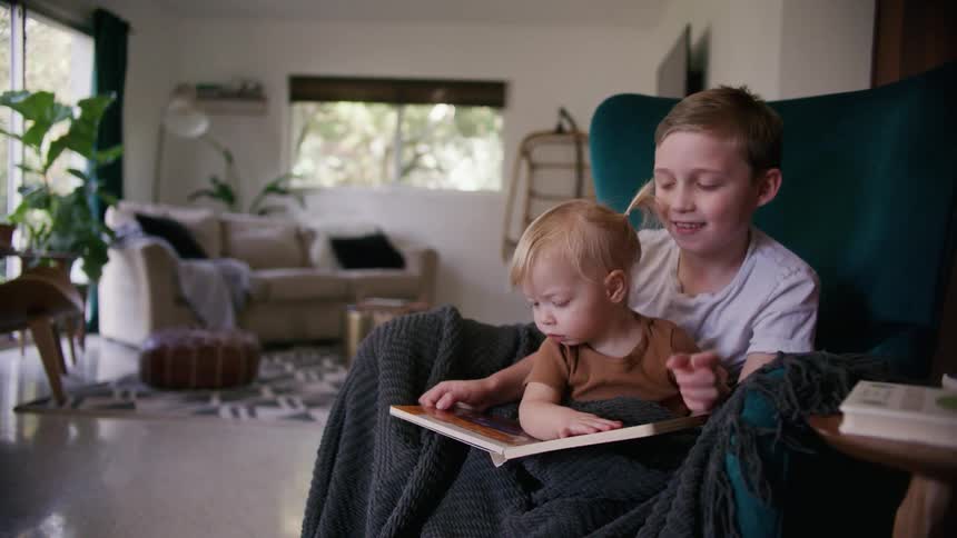 A young boy helps his toddler sister look through a picture book