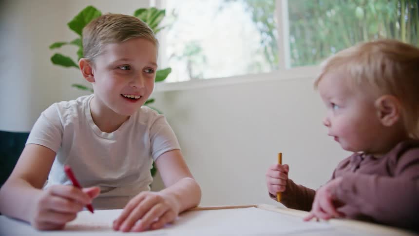 A young boy and toddler girl sit at a table coloring together