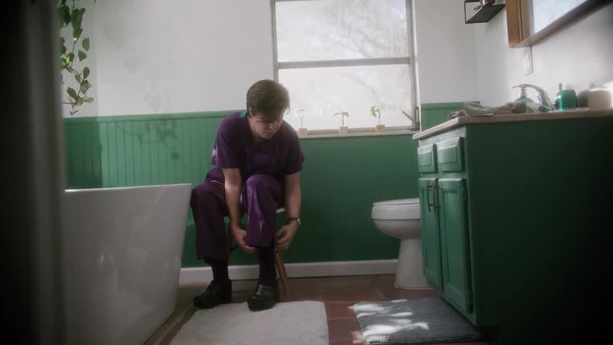 A woman puts her shoes on in a bathroom at home