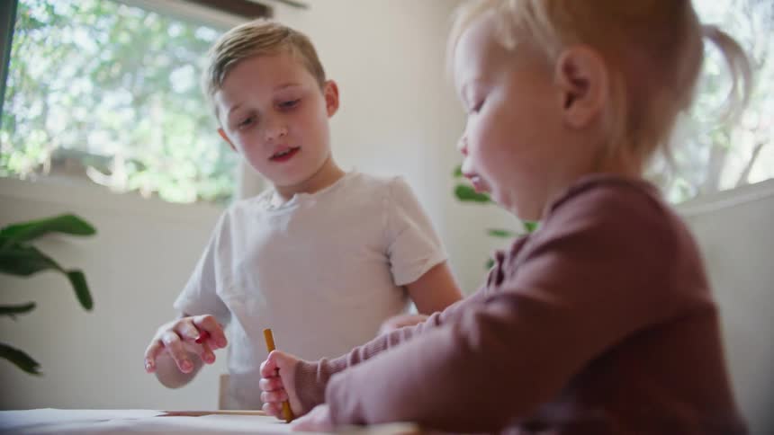 A young boy and toddler girl sit together coloring at a table