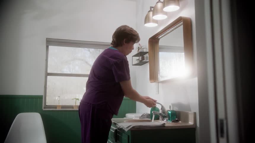 A home health nurse walks to the bathroom sink where she washes her hand