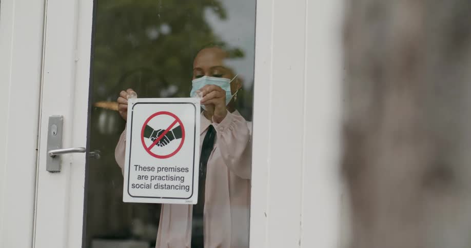 A business owner hangs a sign in the doorway promoting social distancing