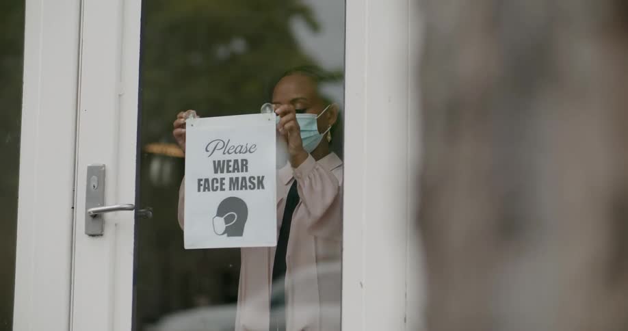 A business owner places a sign on the door with a picture showing that face masks are required